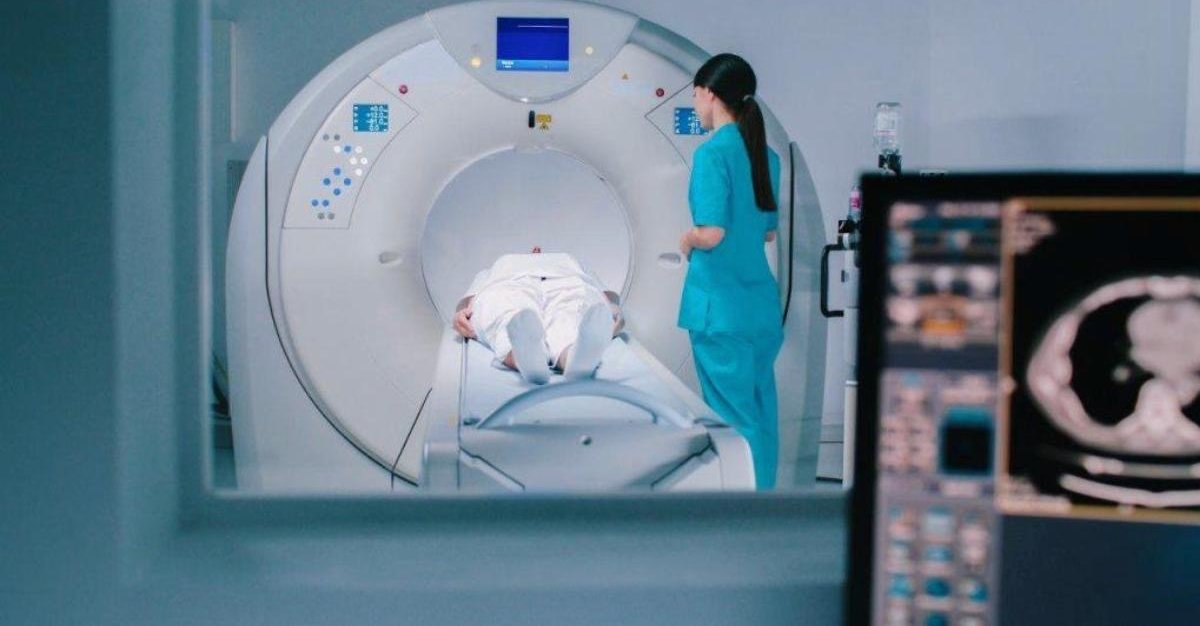 A clinician operating a CT scanner as a patient undergoes medical imaging